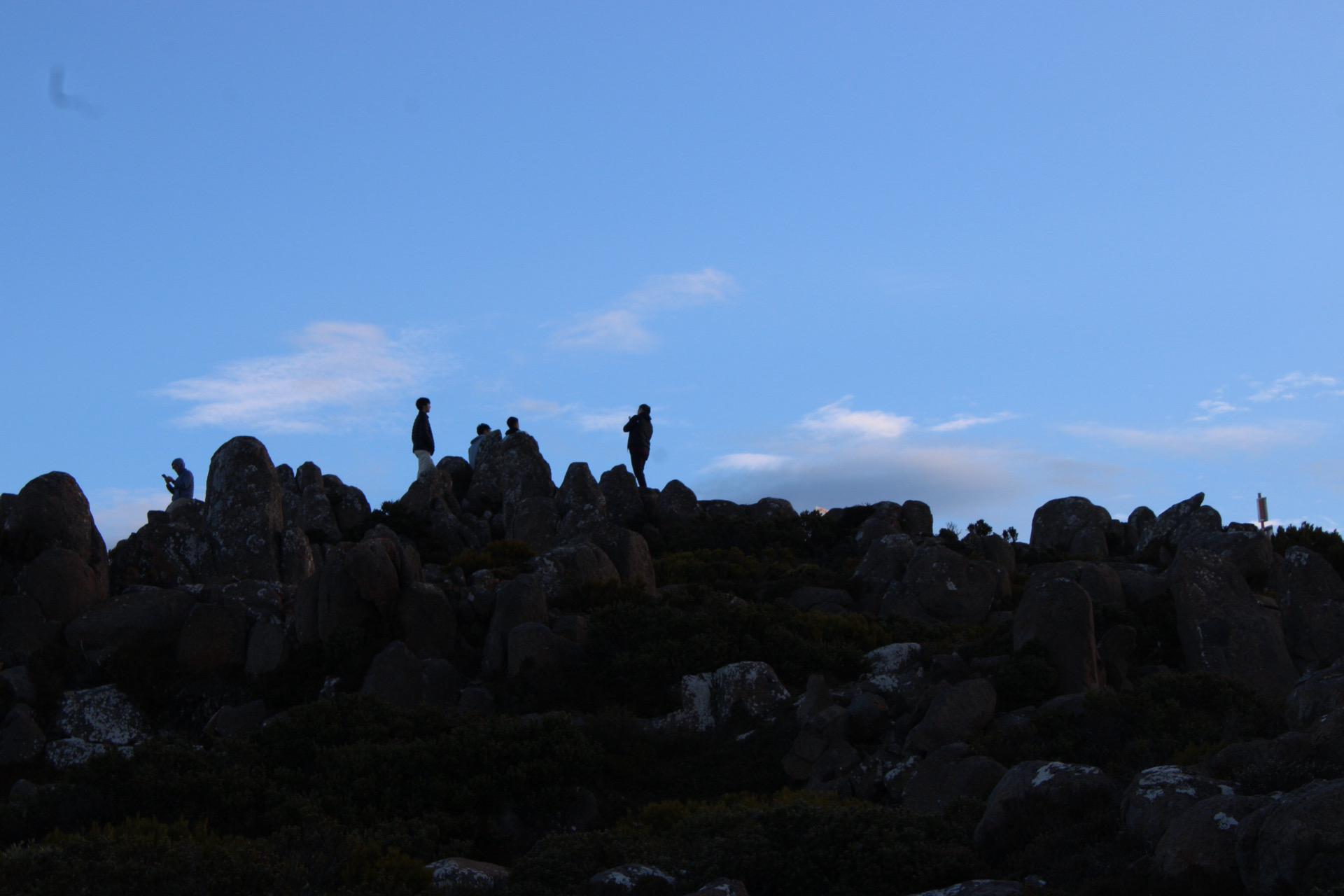 Small people standing among dark rock formations beneath an open blue sky
