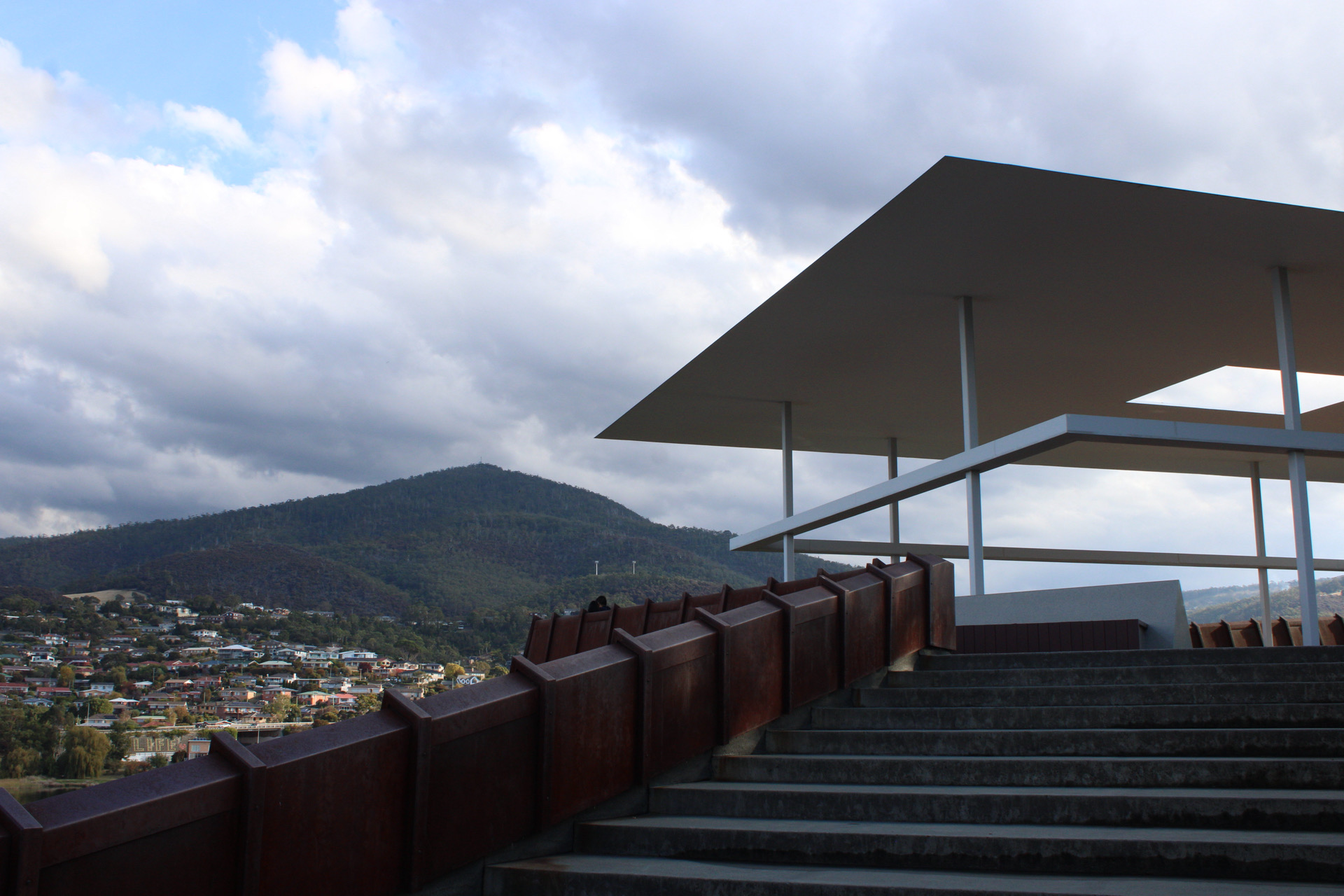 A staircase and rust colored wall connecting a geometric roof plane to the surrounding mountain