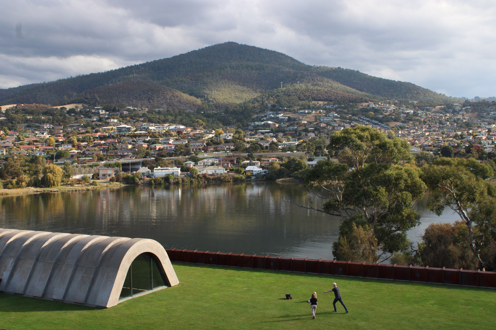 A broad view across water and a mountain with distant figures on a green lawn
