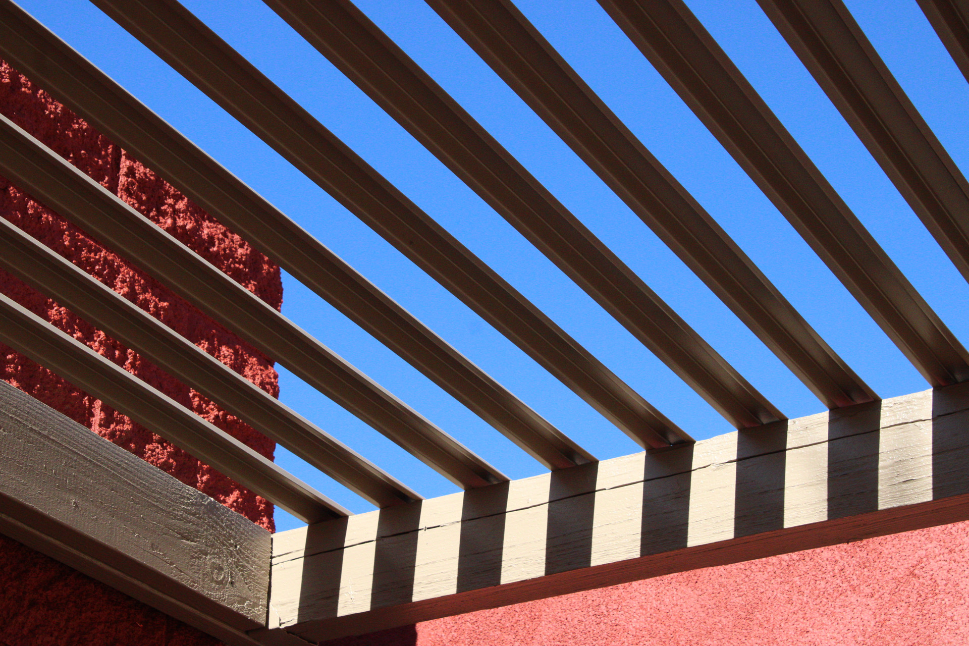 Geometric beams, red surfaces and repeated shadows against a clear blue sky